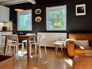 A modern living room with a wooden dining table, white chairs, a brown leather sofa, and a small side table. - Cozy Durbuy Chalet With Fireplace (Rendeux)