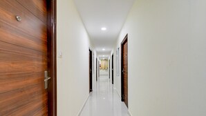 A corridor with wooden doors, white walls, and a shiny floor. - Deluxe Munagala Arcade (Hyderabad)