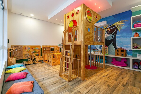 Una sala de juegos infantil con una casita de madera, un mural y diversos juegos.