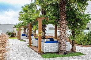 Un espace extérieur aménagé, abrité et doté de mobilier en osier blanc et de coussins bleus, entouré de palmiers et de plantes.