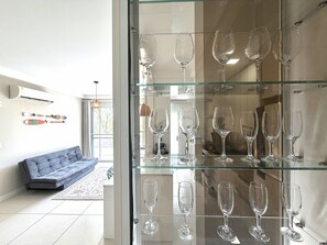 Un salon moderne avec une vitrine où sont exposées des verres à vin, un canapé gris et des paires de skis accrochées au mur.
