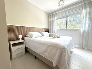 Un dormitorio moderno con cama, mesita de noche y ventana con cortinas.
