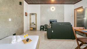 Quarto de hotel com cama, sofá, mesa de jantar, geladeira e ventilador.