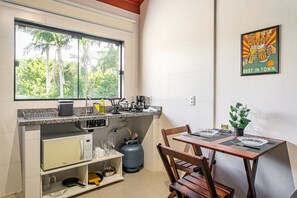 A kitchen with a window, a table with chairs, a microwave, a gas cylinder, and a framed poster on the wall.