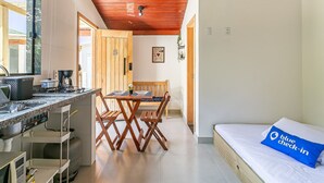 Een compacte kamer met een kitchenette, een eethoek en een bed met een blauw kussen.
