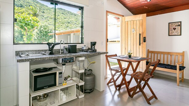 Een compacte keuken met een magnetron, gasfornuis en een groot raam met uitzicht op een groen landschap.