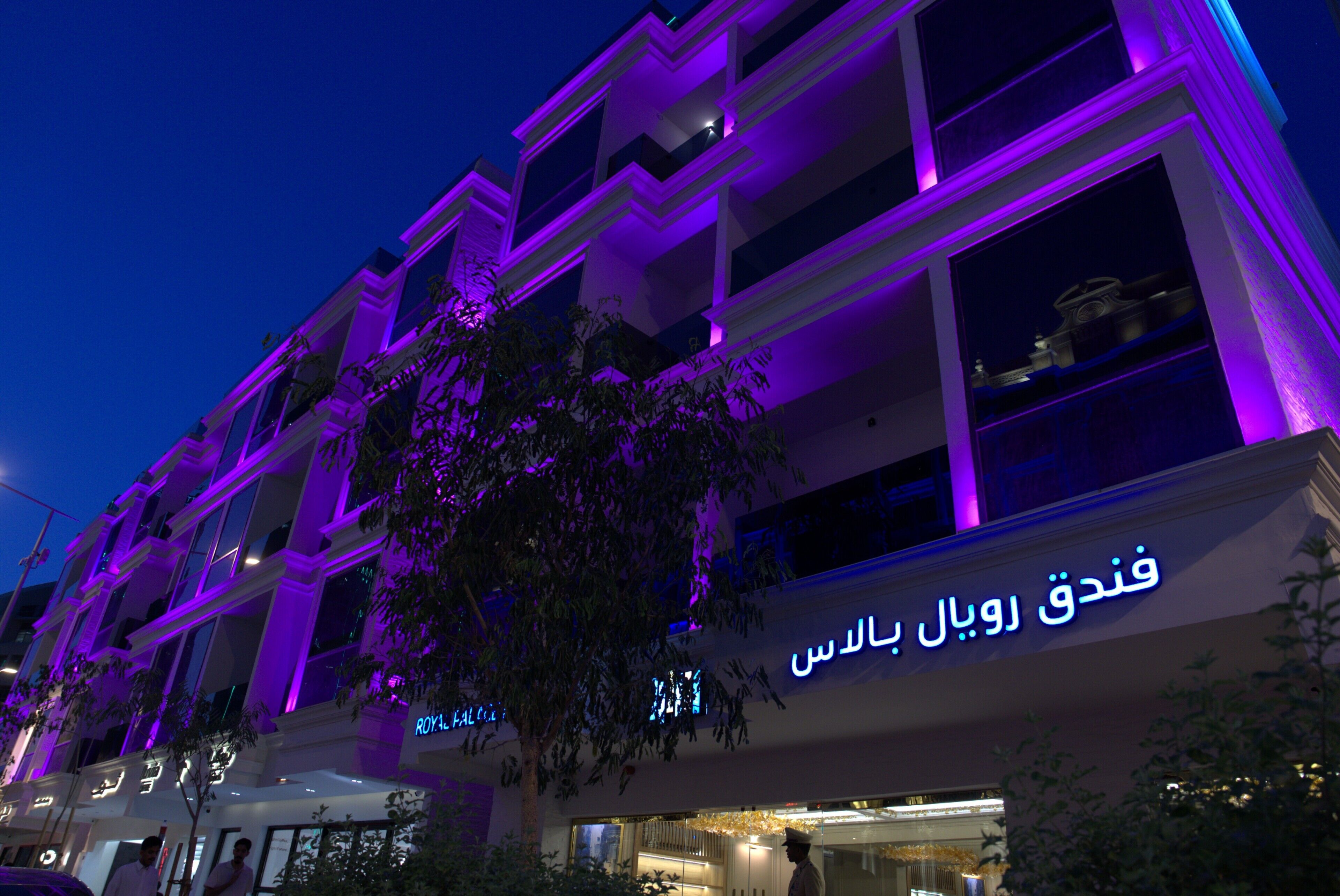 Un hotel de varios pisos con letreros iluminados, balcones y un árbol en la fachada.