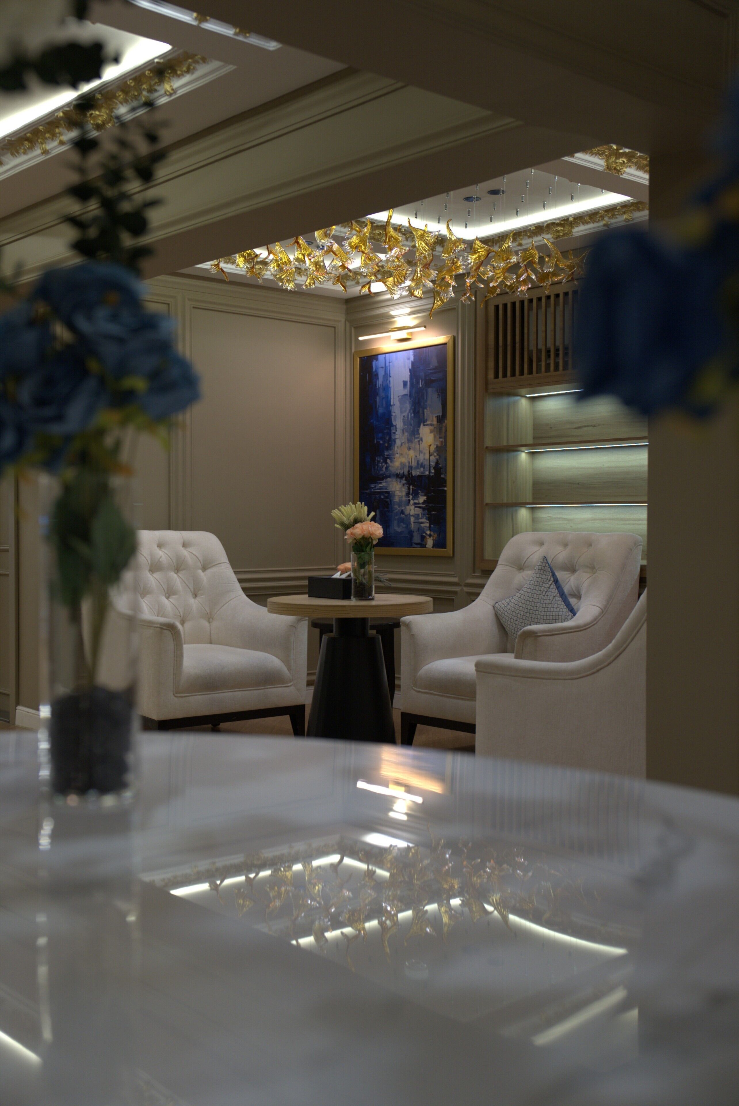 A modern interior with two white upholstered chairs, a round table, and a vase with flowers.