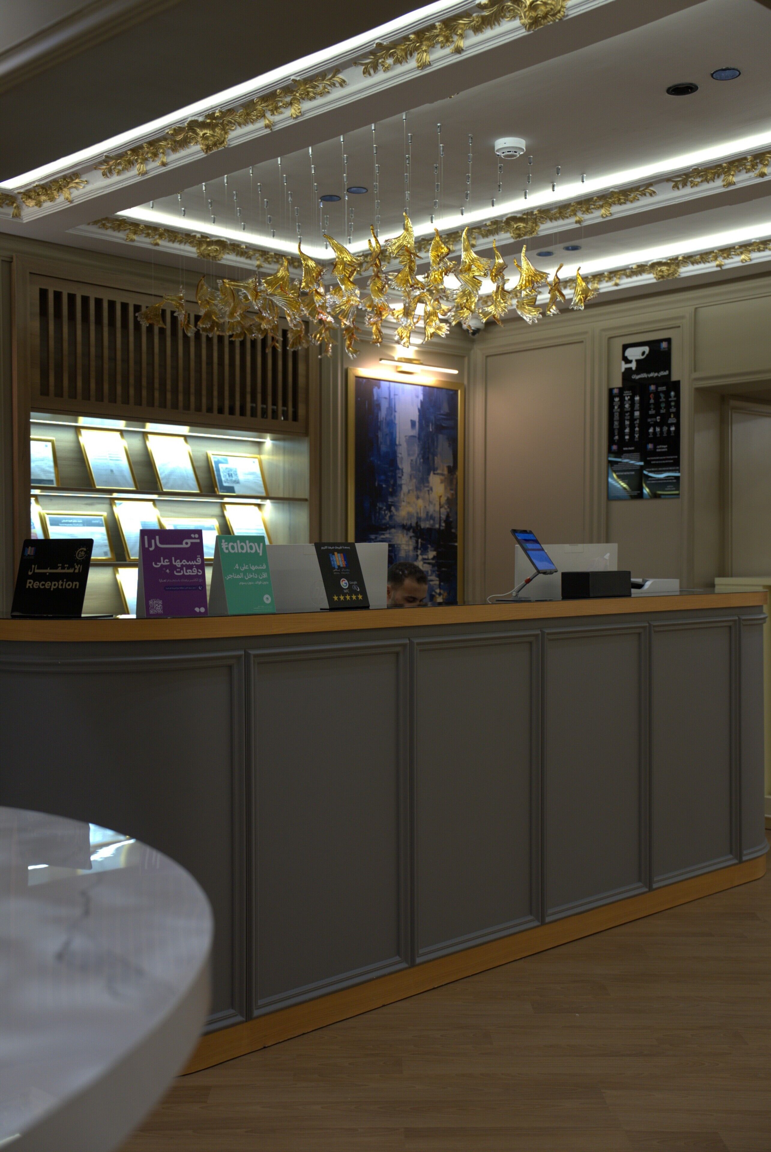 A reception desk with a modern chandelier, a digital display, and a wall-mounted screen.