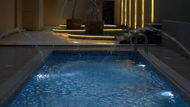 Une piscine dotée de jets d’eau, entourée d’un bâtiment moderne agrémenté de bandes lumineuses verticales.