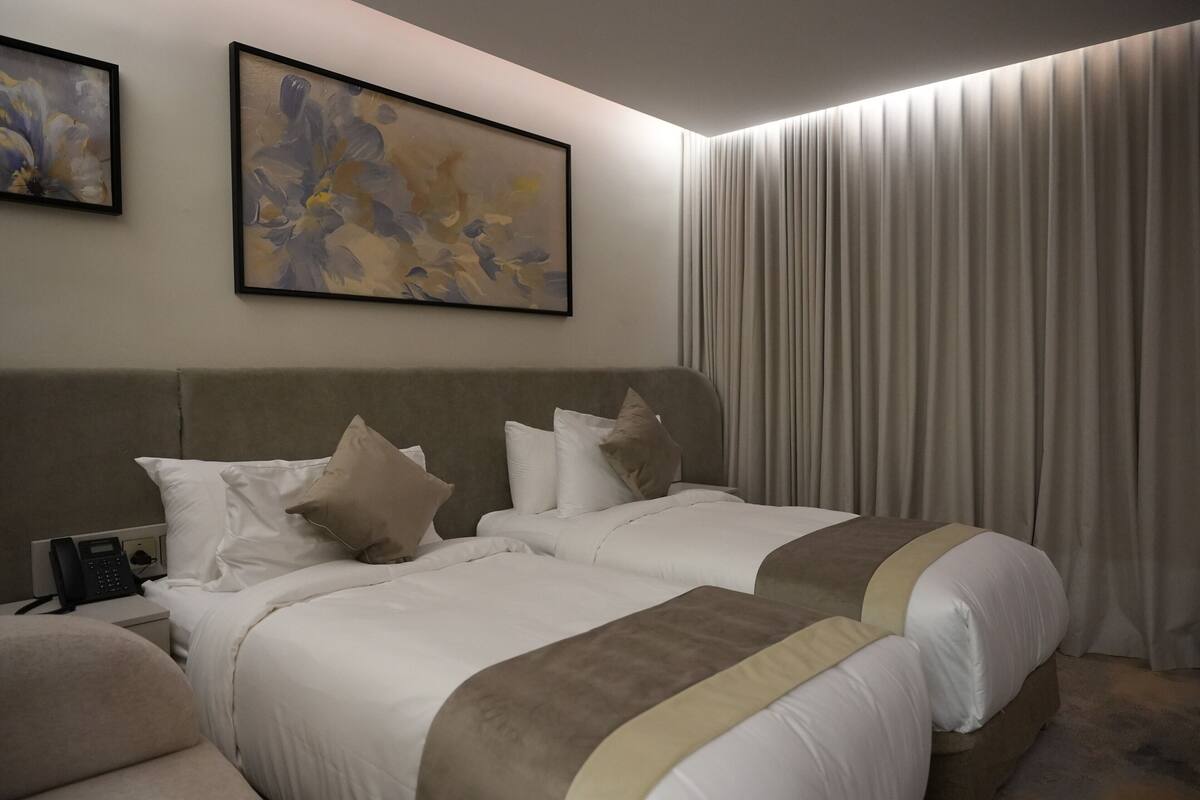 A hotel room with two beds, a telephone, and artwork on the wall.