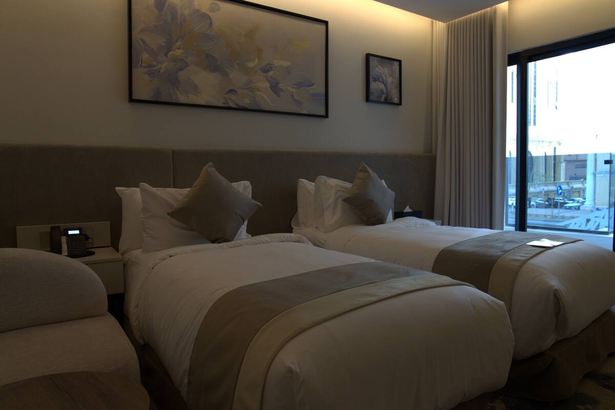 A hotel room with two beds, a bedside table with a phone, and artwork on the wall.