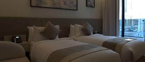 A hotel room with two beds, a bedside table with a phone, and artwork on the wall.