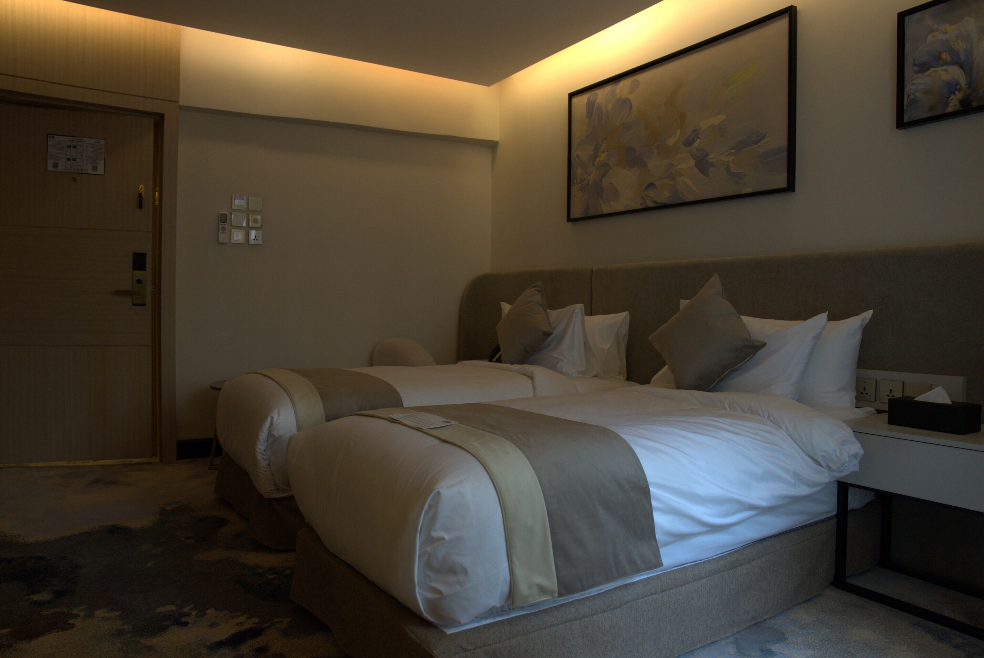 Habitación de hotel con dos camas, una mesita de noche, una lámpara y un cuadro en la pared.