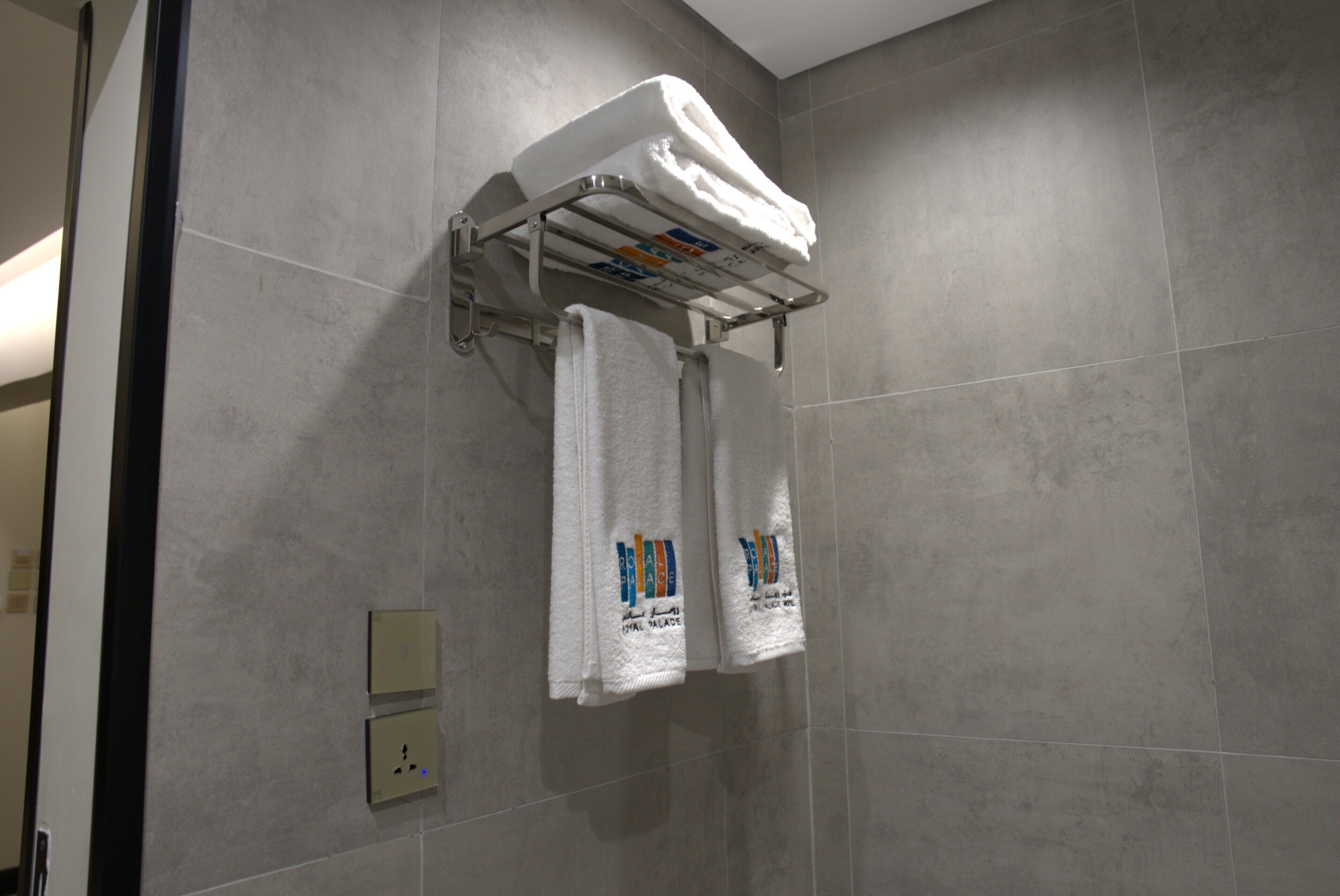 A bathroom with grey tiles, a towel rack with two towels, and a power outlet.