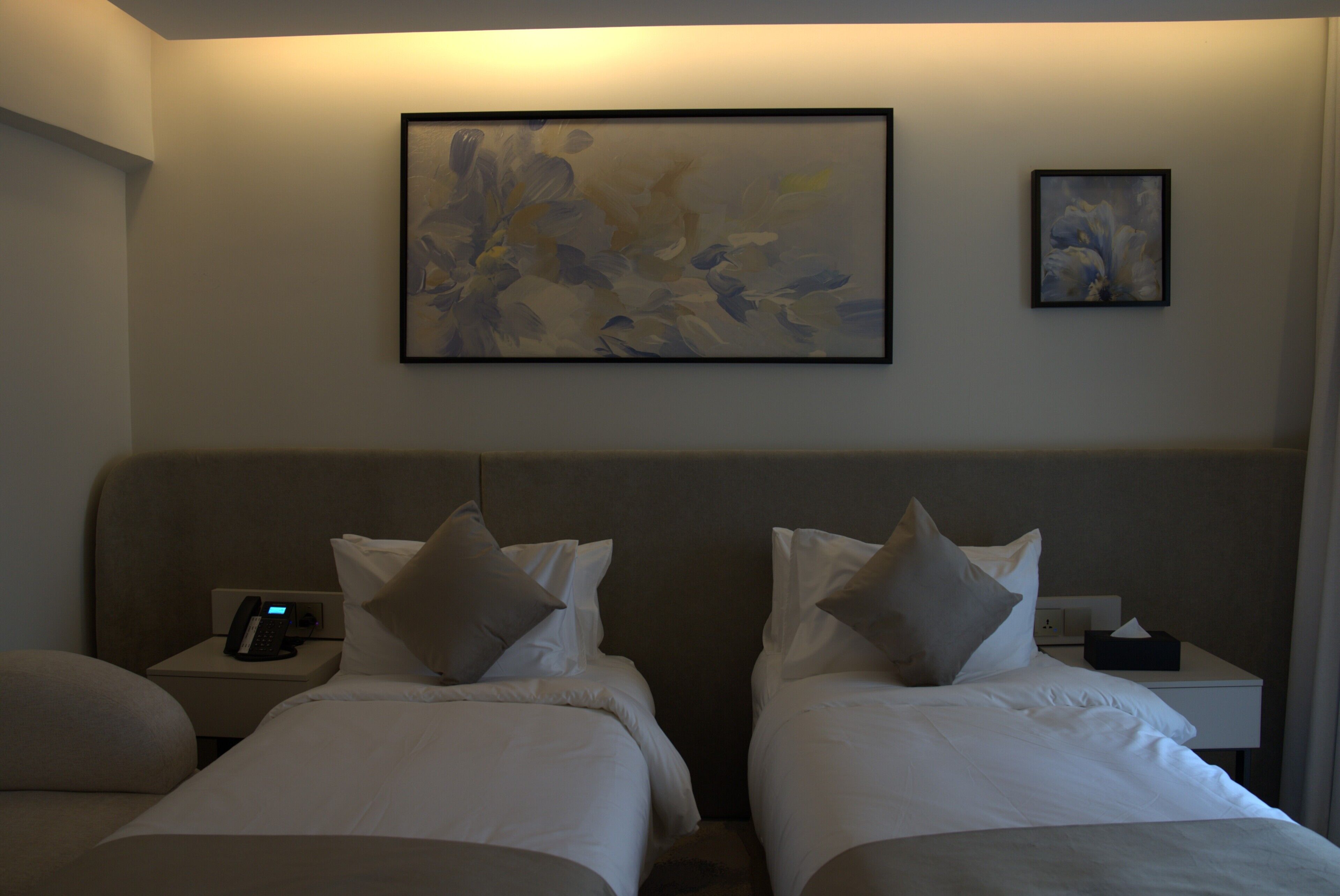 Ein Hotelzimmer mit zwei Betten, einem Nachttischtelefon, einem Beistelltisch und einem gerahmten abstrakten Gemälde an der Wand.