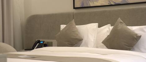 A hotel room with a bed, pillows, a bedside table with a phone, and a painting on the wall.
