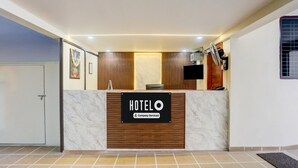 Una recepción de hotel con mostrador de mármol, paneles de madera, un televisor de pantalla plana y un cartel que indica que es un hotel de servicios empresariales.