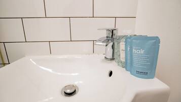A white bathroom sink with a chrome faucet, a blue toiletry bag labeled 'travelcare essentials,' and a tiled wall in the background.
