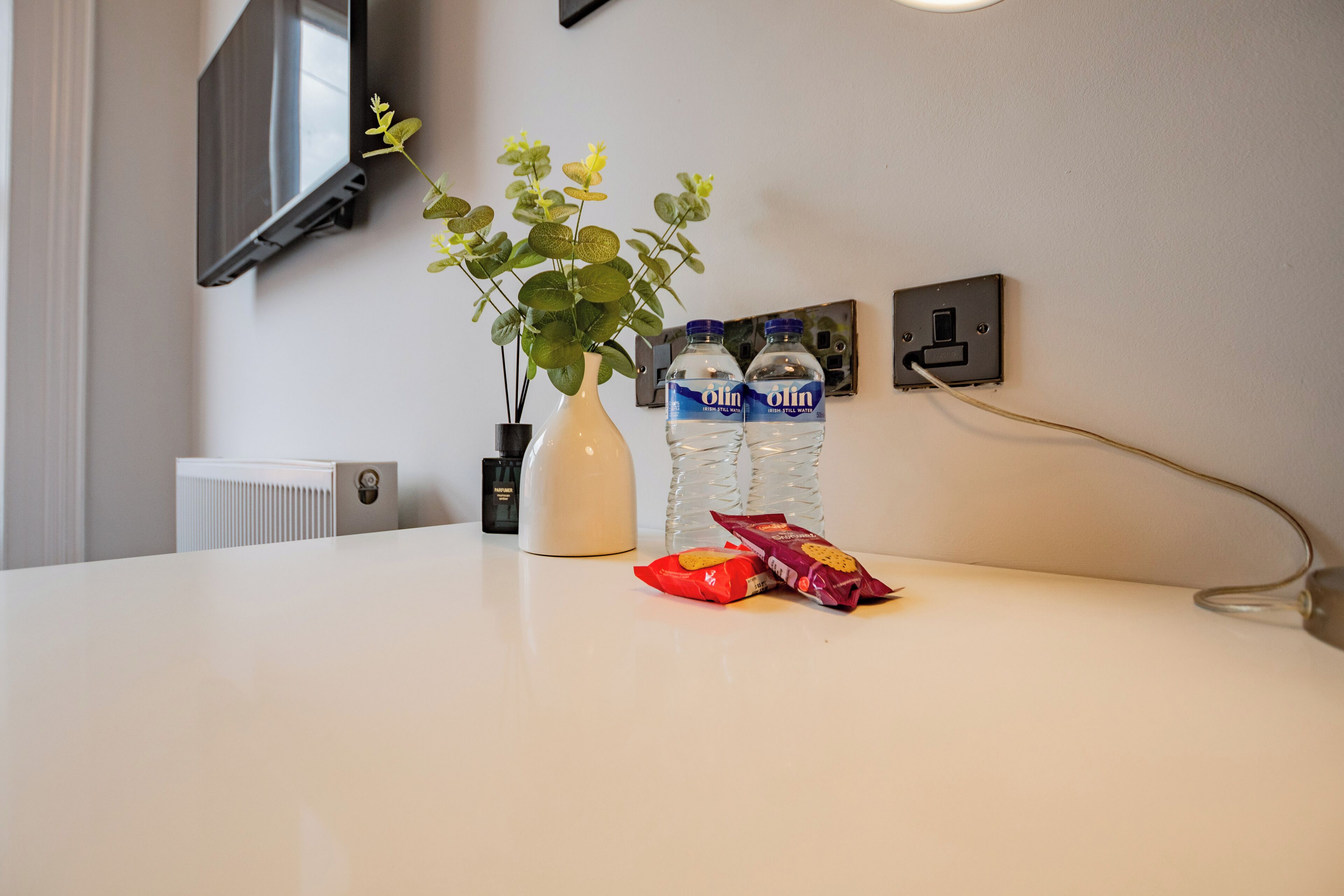 A white table with a white vase, two water bottles, and two snack packets.