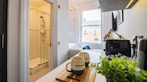 A modern bathroom with a glass shower, a wooden tray with mugs, and a view of the city through a window. - Modern Suite 47 Grove Park | WiFi & TV (Dublin)