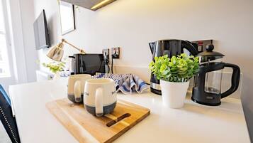 A kitchen with a coffee maker, two mugs, a cutting board, a potted plant, and a striped cloth.