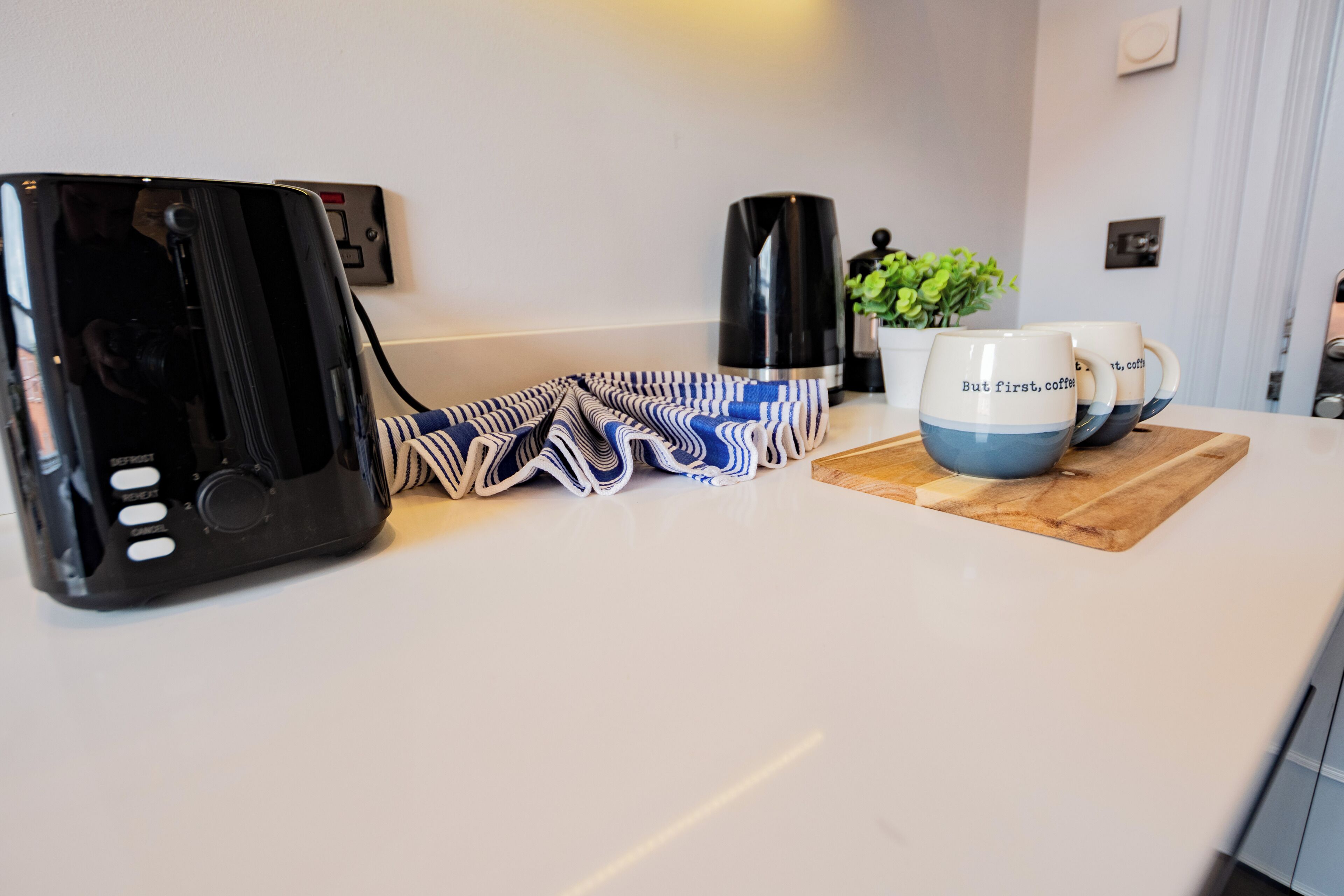 Una encimera de cocina con una cafetera, una planta y un juego de tazas.