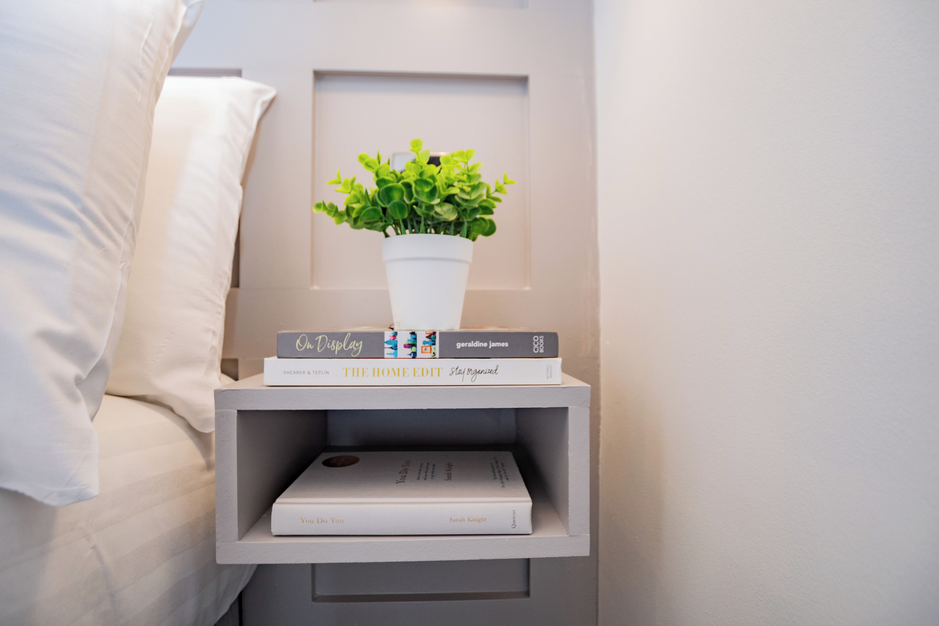 A bedside table with a potted plant, a stack of books, and a small shelf.