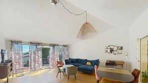 Un'ampia zona giorno con divano, tavolo da pranzo e sedie, una grande finestra con tende e un lampadario.