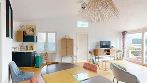Un ampio soggiorno con un tavolo grande, posti a sedere comodi, una televisione e vista sull'esterno.