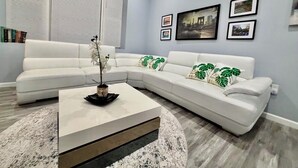 A modern living room with a white sectional sofa, a coffee table, and a large window with blinds.