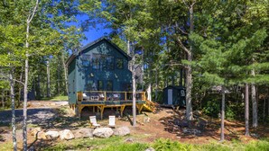 A cabin with a deck, surrounded by trees and a small pond. - Luxury Lakefront Cabin in Hope - Close to Camden & Rockland (Hope)