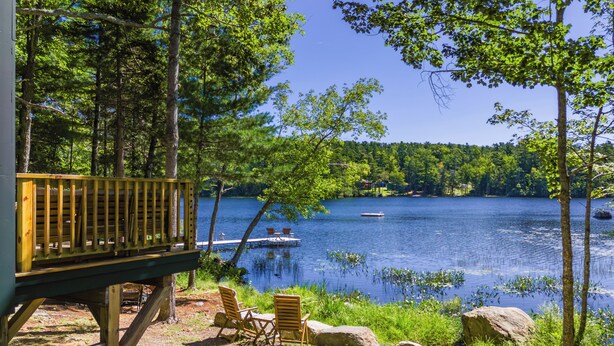 A wooden deck with chairs overlooking a lake, surrounded by trees. - Luxury Lakefront Cabin in Hope - Close to Camden & Rockland (Hope)