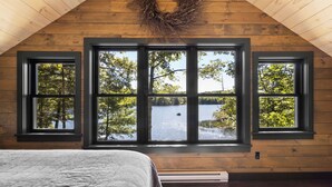 A bedroom with a large window, a bed, and a checkered rug. - Luxury Lakefront Cabin in Hope - Close to Camden & Rockland (Hope)