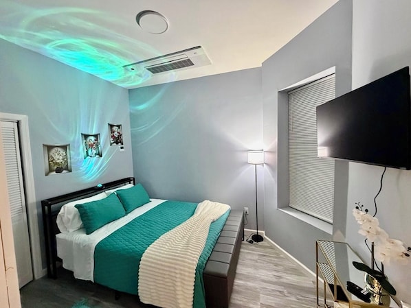 Une chambre à coucher avec un lit, une télévision, une lampe et un projecteur au plafond.