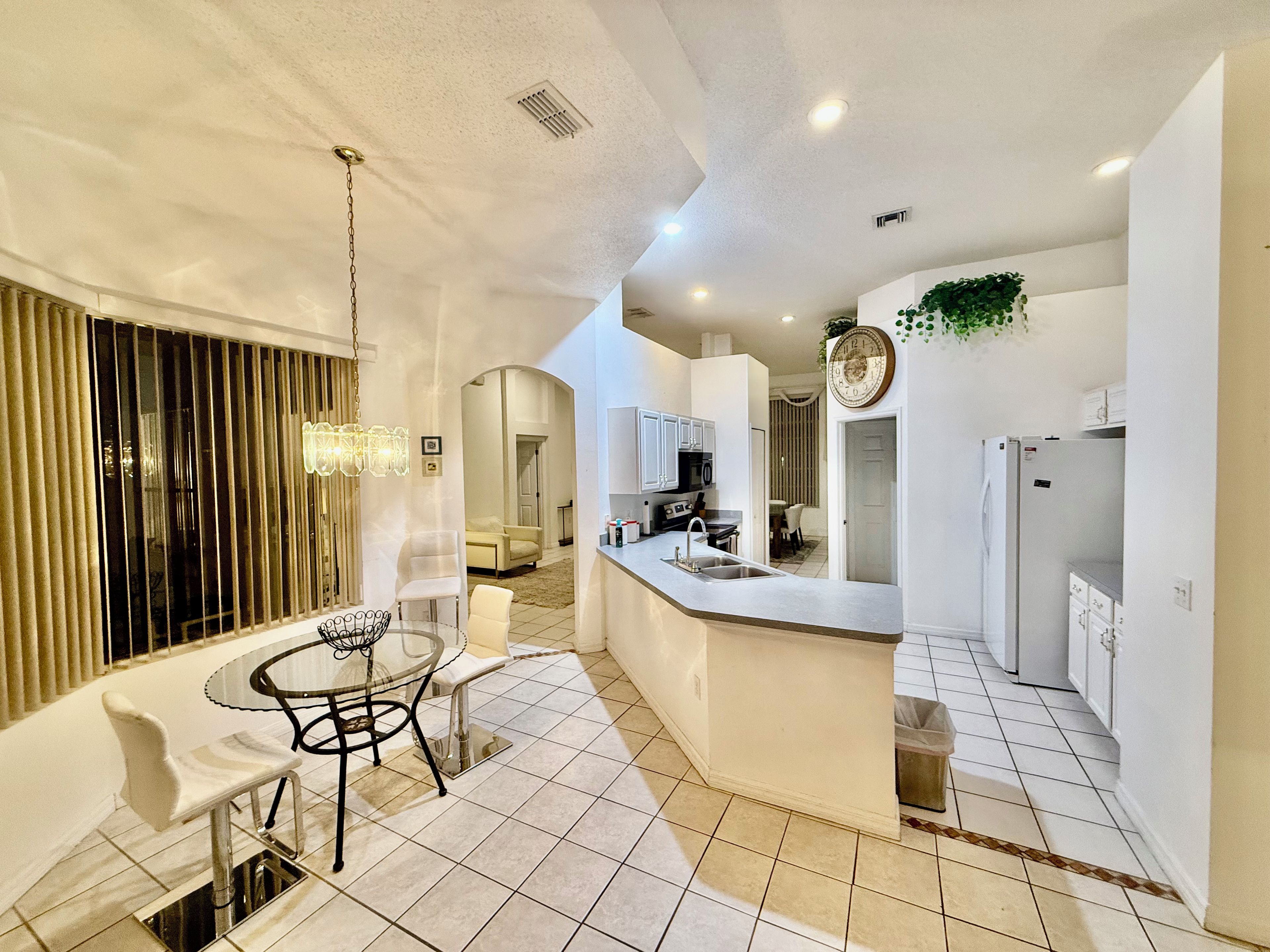 A modern kitchen with a central island, white cabinetry, and a dining area with a glass table and chairs.
