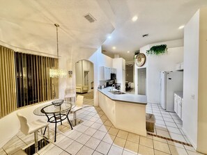 Una cocina moderna con una isla central, armarios blancos y una zona de comedor con mesa y sillas de vidrio.