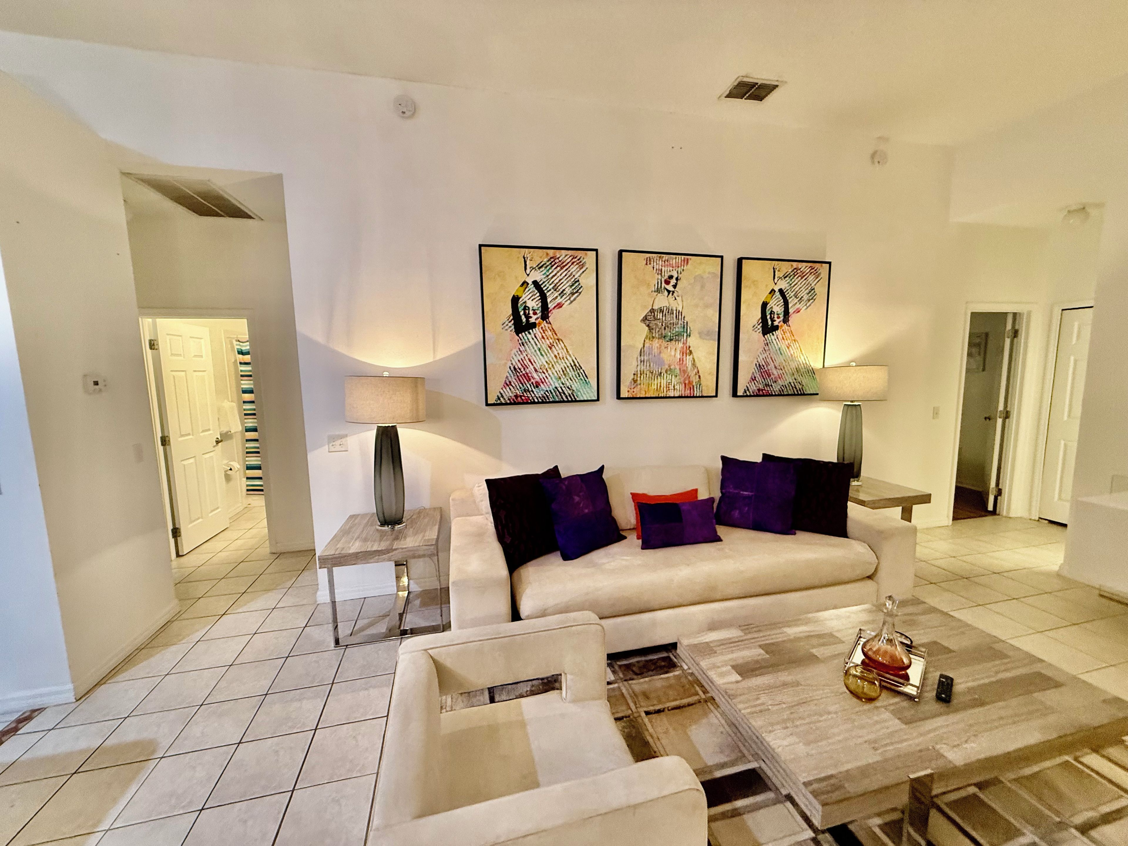 Sala de estar com sofá, mesa de centro e luminária. Há três quadros na parede.