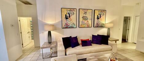 Una sala de estar con un sofá, una mesa de centro y una lámpara. Hay tres cuadros en la pared.