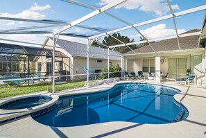 A swimming pool with a sunshade structure, lounge chairs, and a covered patio area. - Grand Luxury Grove 4BR Home Near Disney (Four Corners)