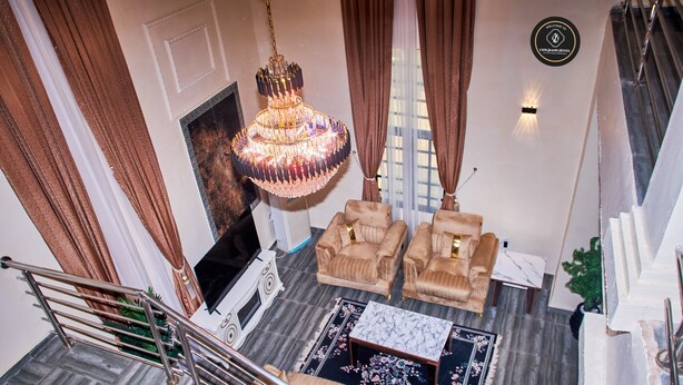 A spacious living area with a chandelier, sofas, a coffee table, and a staircase. - Ozigrand Hotel (Benin City)