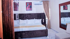 A bedroom with a bed, a chair, a mirror, and artwork on the walls. - Ozigrand Hotel (Benin City)