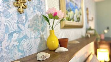A wooden shelf with decorative shells, a yellow vase with flowers, and a framed picture on a wall with a blue and white pattern.
