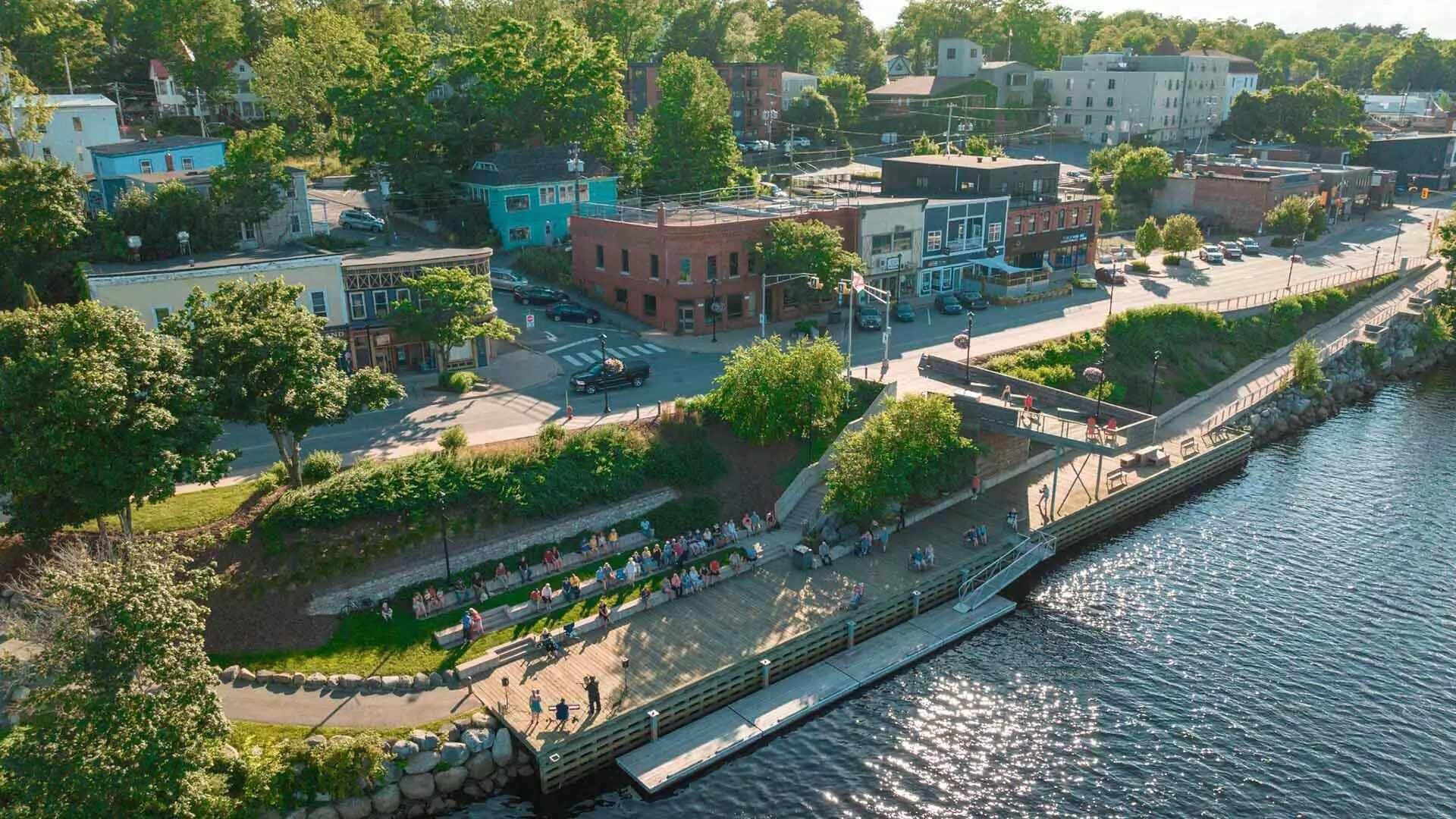 Vista aerea di una cittadina lungo il fiume, con edifici, una passeggiata pedonale e un ponte.