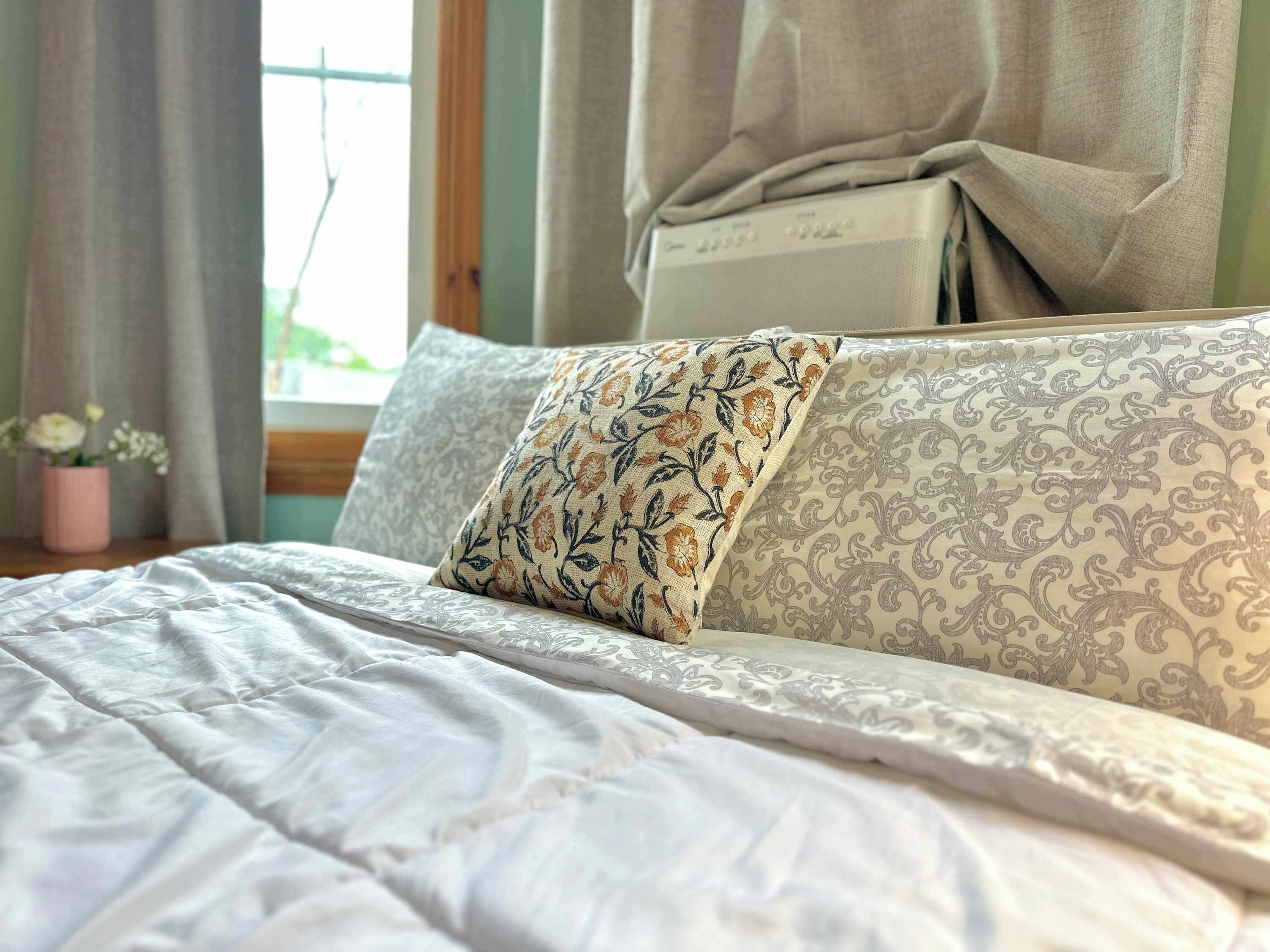 A bed with a floral pillow, a patterned pillow, and a white comforter.