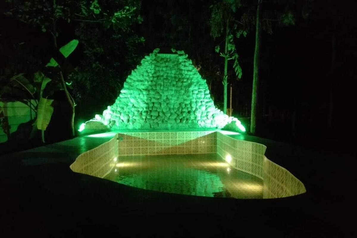 Una fuente con una estructura de piedra iluminada por luces verdes, rodeada de árboles.
