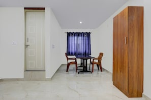 Um quarto com porta, uma mesa com cadeiras, uma janela com cortinas e um guarda-roupa.