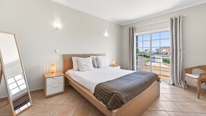Een hotelkamer met een groot bed, een nachtkastje met een lamp, een stoel en uitzicht op buiten.