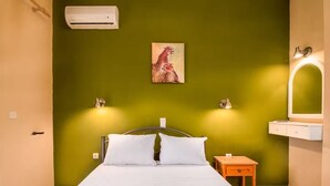 Quarto com uma cama, pintura de um chita, duas luminárias na parede, um espelho e uma pequena mesa de cabeceira de madeira.