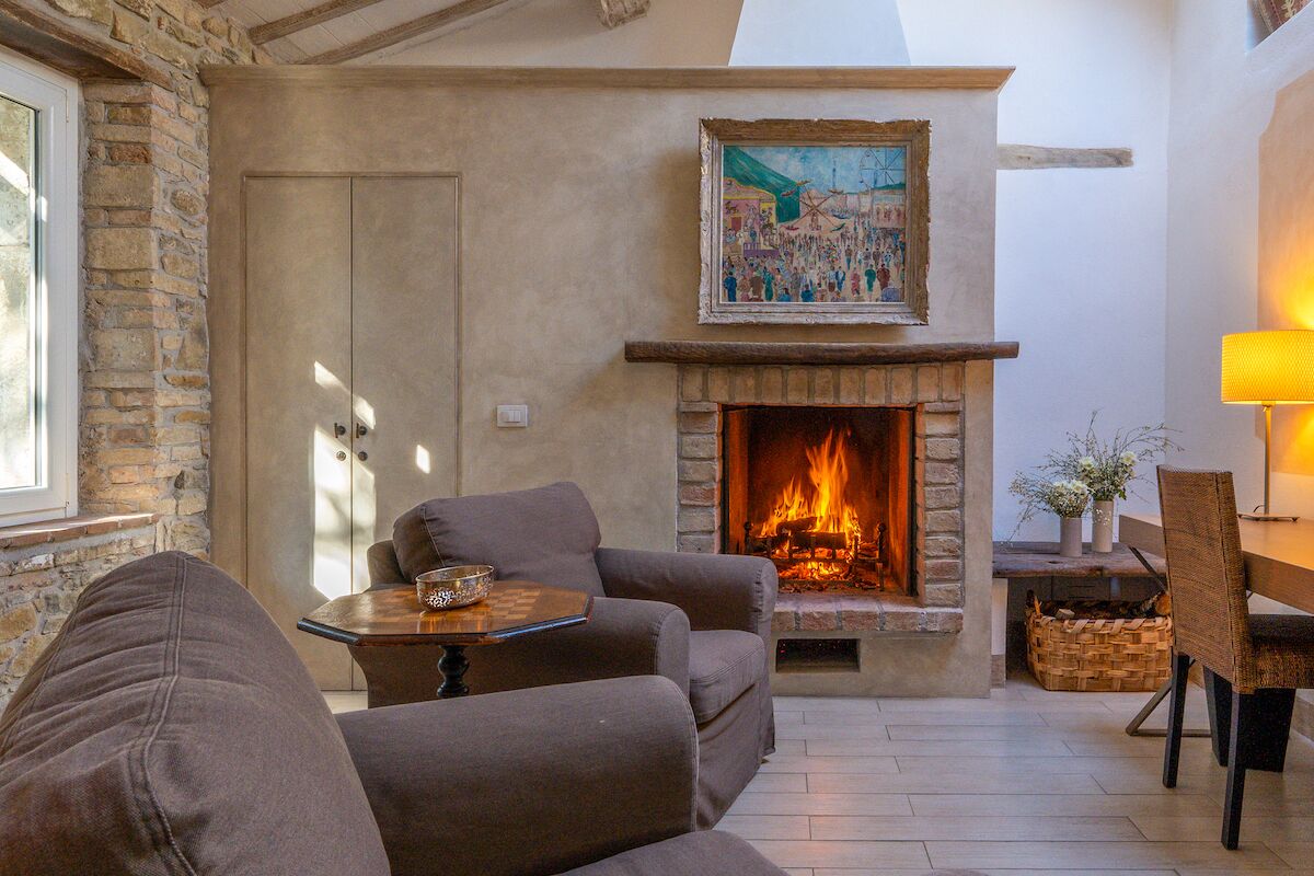 A cozy living room with a fireplace, stone walls, and a painting above it.